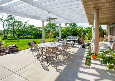 A concrete back patio with large pergola and garden area